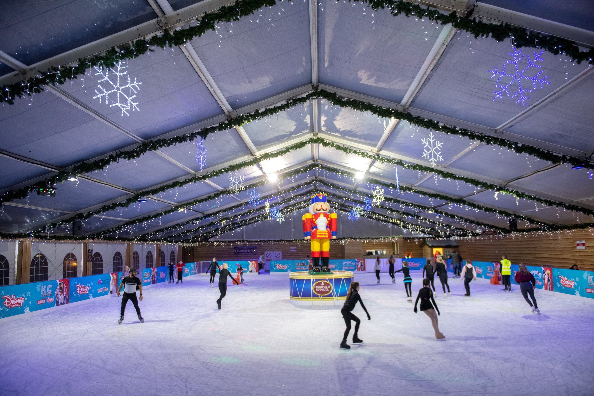 skaters skating on the real winter ice rink at Bluewater Shopping Centre. The rink barriers are branded with the sponsor Disney and the focal point is two large nutcrackers in the middle of the ice. 