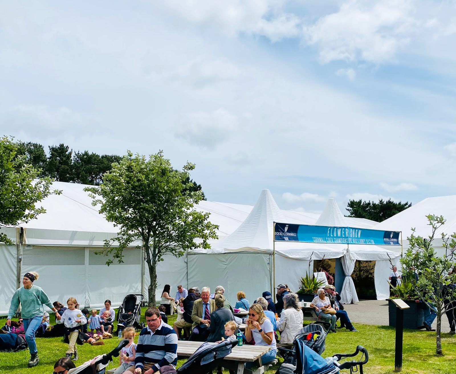 Flower tent at Royal Cornwall Show. Surrounded by people attending the show sat on benches and on the grass enjoying picnics. 