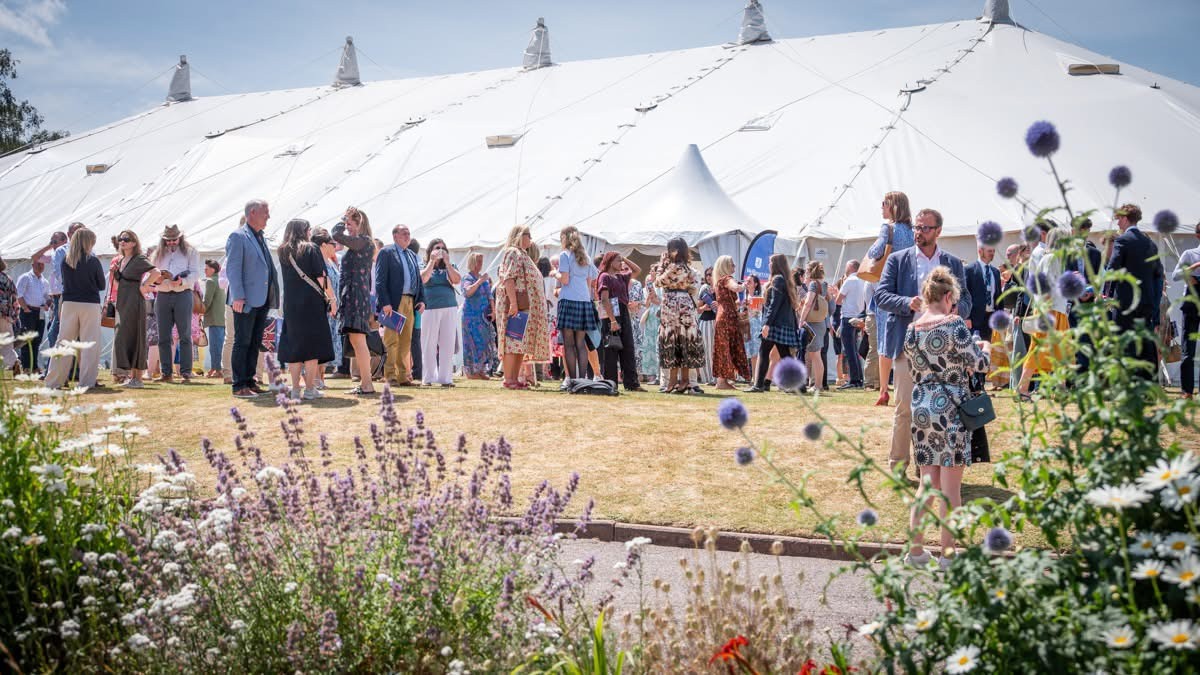 Wellington School Senior Prize Giving Event. People are gathered outside the traditional marquee  in the summer sun and beautiful range of flowers at the front. 