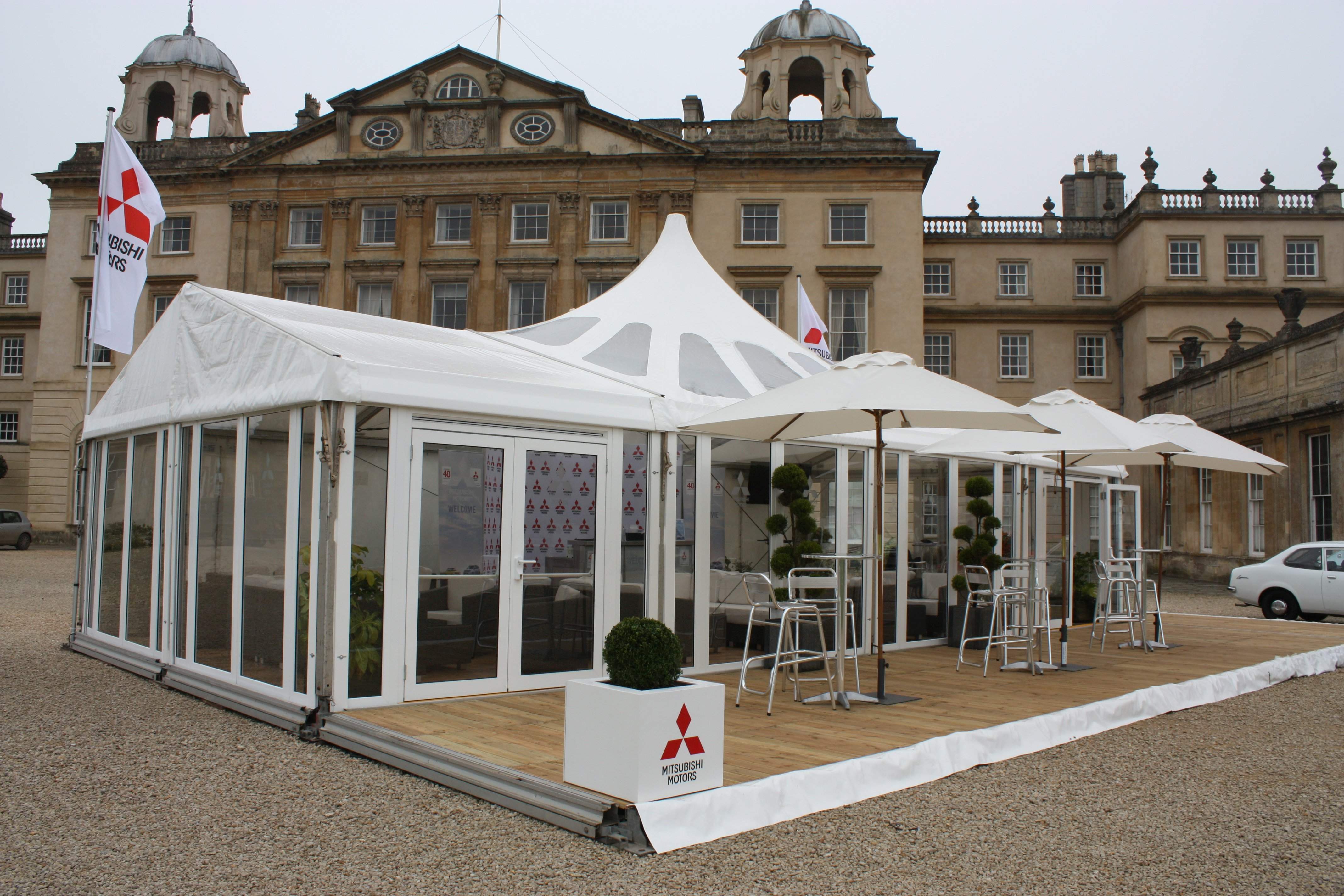 Clear solid sided marquee with a semi clear peaked roof on a floor with external decking for Mitsubishi Motors in front of Badminton House