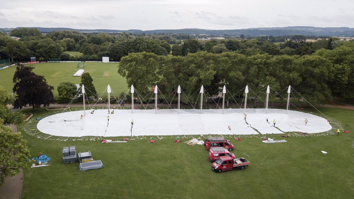 The build of a traditional Danco tent for the Taunton Flower Show. Workers are putting up the tent on the field with the cricket pitch in the background.