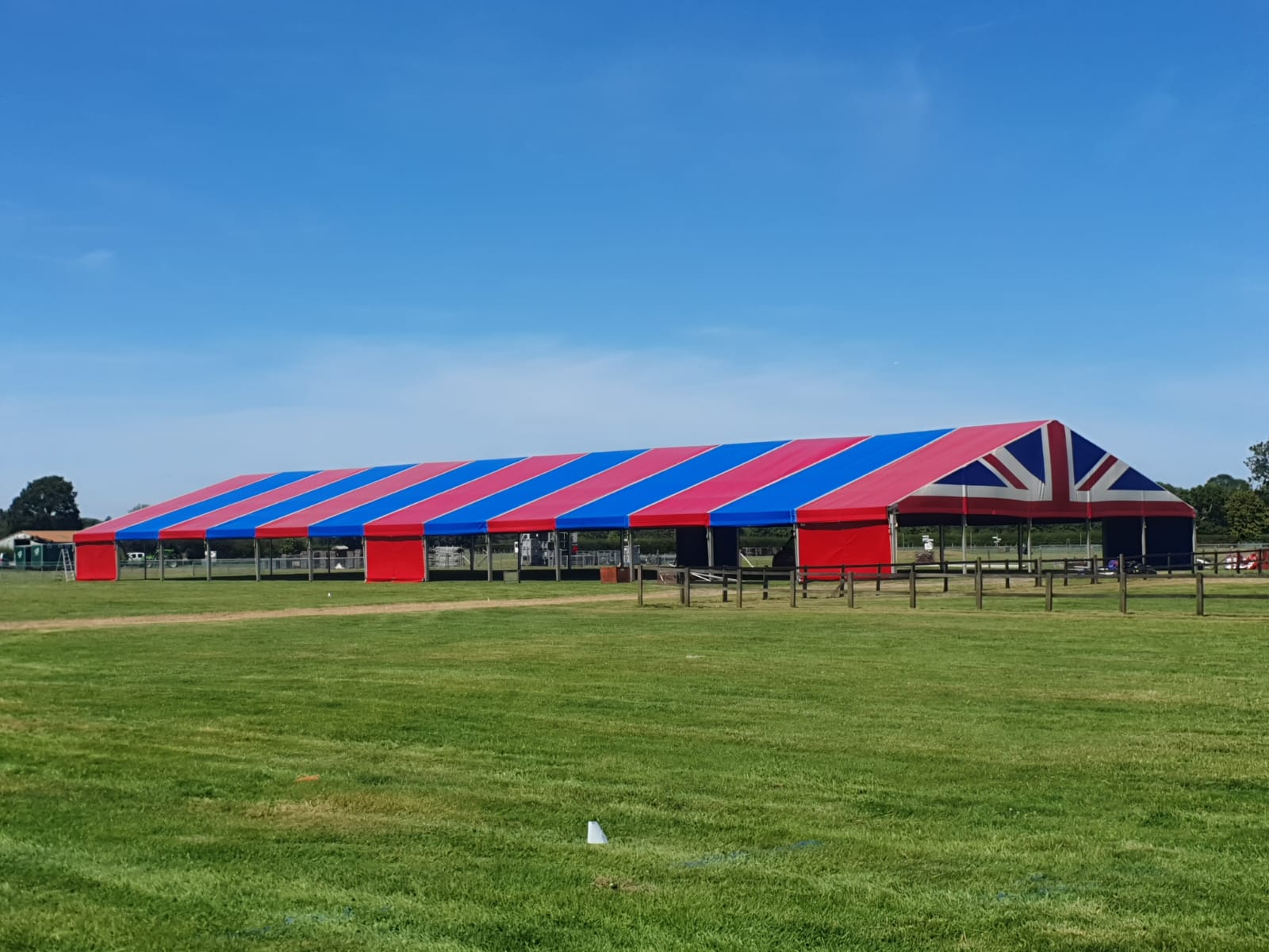 A 65 metre long clearspan marquee. The roofs are red and blue and the gable end of the marquee cover is a Union Jack. A clear sky and positioned in the field in the Edenbridge and Oxted Agriculture Show. 