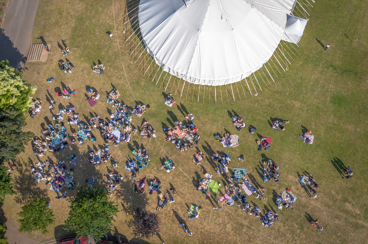 A drone image of part of a traditional marquee in a school field with people enjoying picnic on the grass.